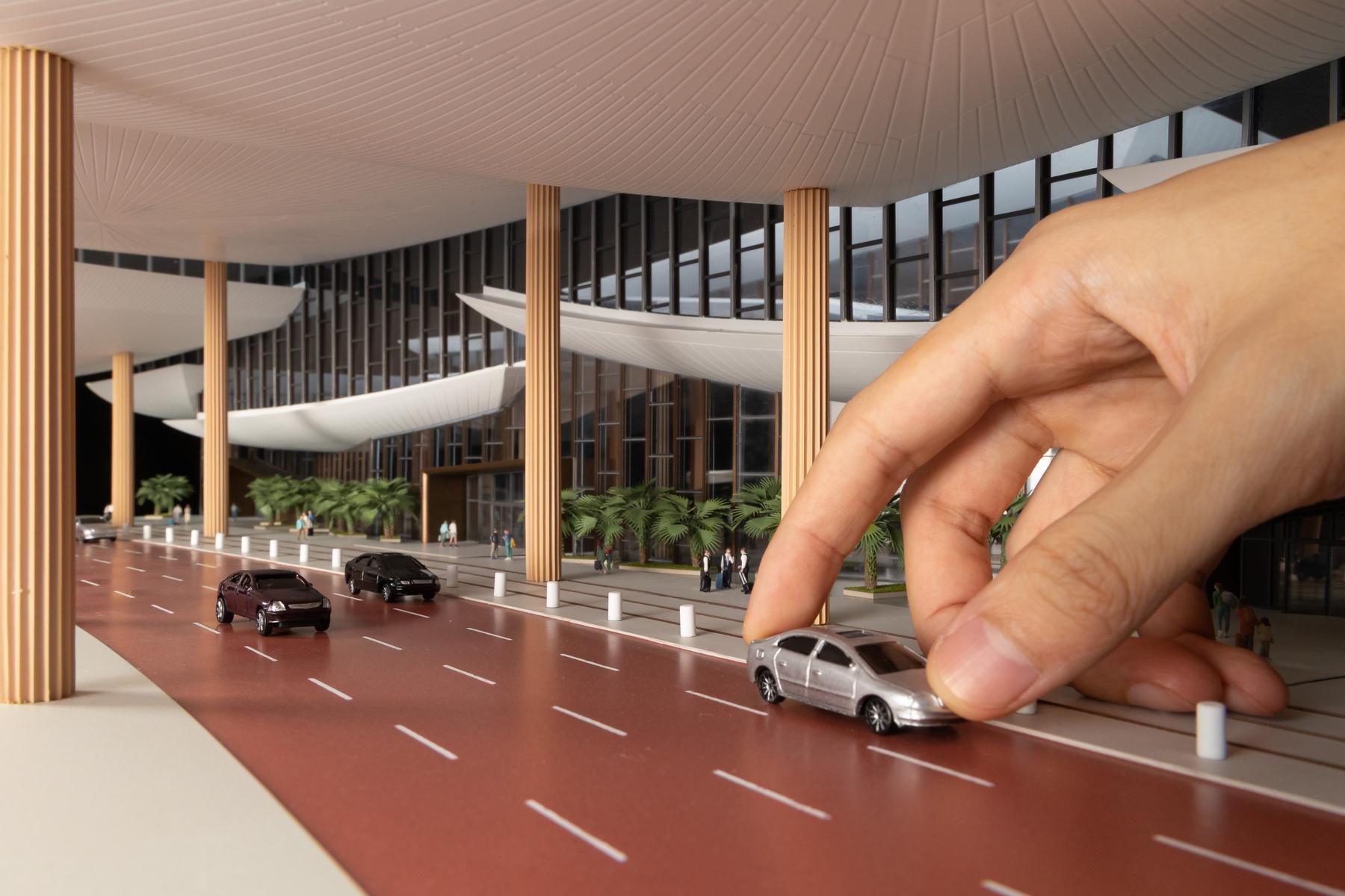A model maker's hand placing a miniature car on an airport terminal scale model