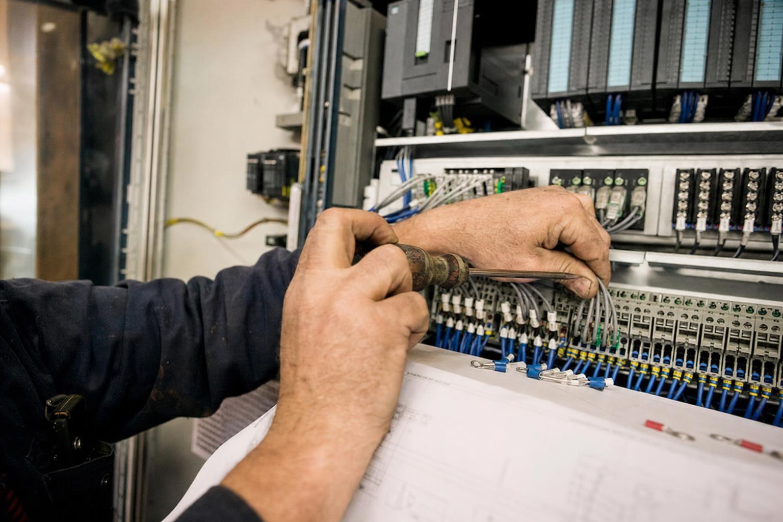 An engineer's hands wiring a PLC control cabinet